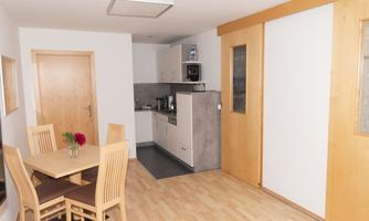 A modern kitchen with a dining table and chairs. The walls are bright, and the room is well-lit.