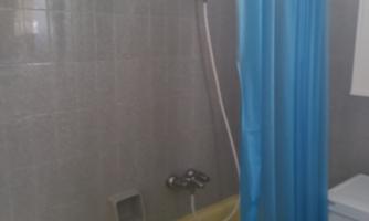 A bathroom with a bathtub, shower curtain, and washing machine. The walls are tiled in light gray.