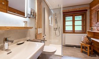 A modern bathroom with wooden paneling and a shower stall. Large windows let in plenty of light and offer a view of the greenery.