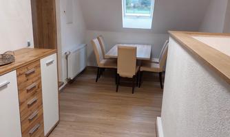A bright hallway with wooden floor and a cozy dining area. A window provides natural light.