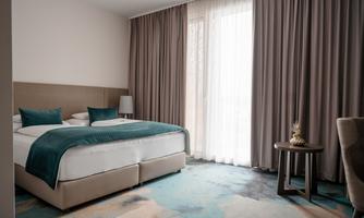 A modern bedroom with a large bed and elegant curtains. The room is bright and friendly designed, with a small table next to the bed.