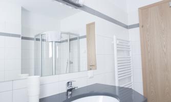 A modern bathroom with a sink and a large mirror. The shower is separated by a glass partition and there is a towel holder as well as a wooden door.