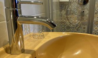 A modern faucet above an orange sink. Tiled walls and a shower cabin are visible in the background.