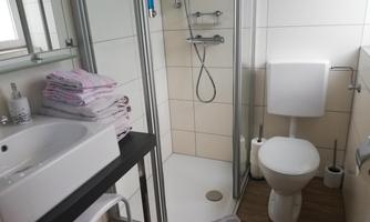 A modern bathroom with a shower, a sink, and a toilet. Towels are neatly stacked on a table.