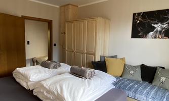A cozy bedroom with two beds and a wooden wardrobe. Decorative pillows in various colors are placed on the sofa.