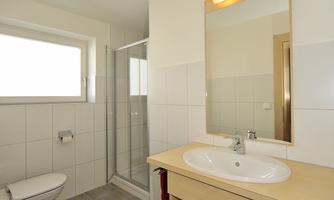 A modern bathroom with bright tiles and a large mirror. There is a shower, a sink, and a toilet.