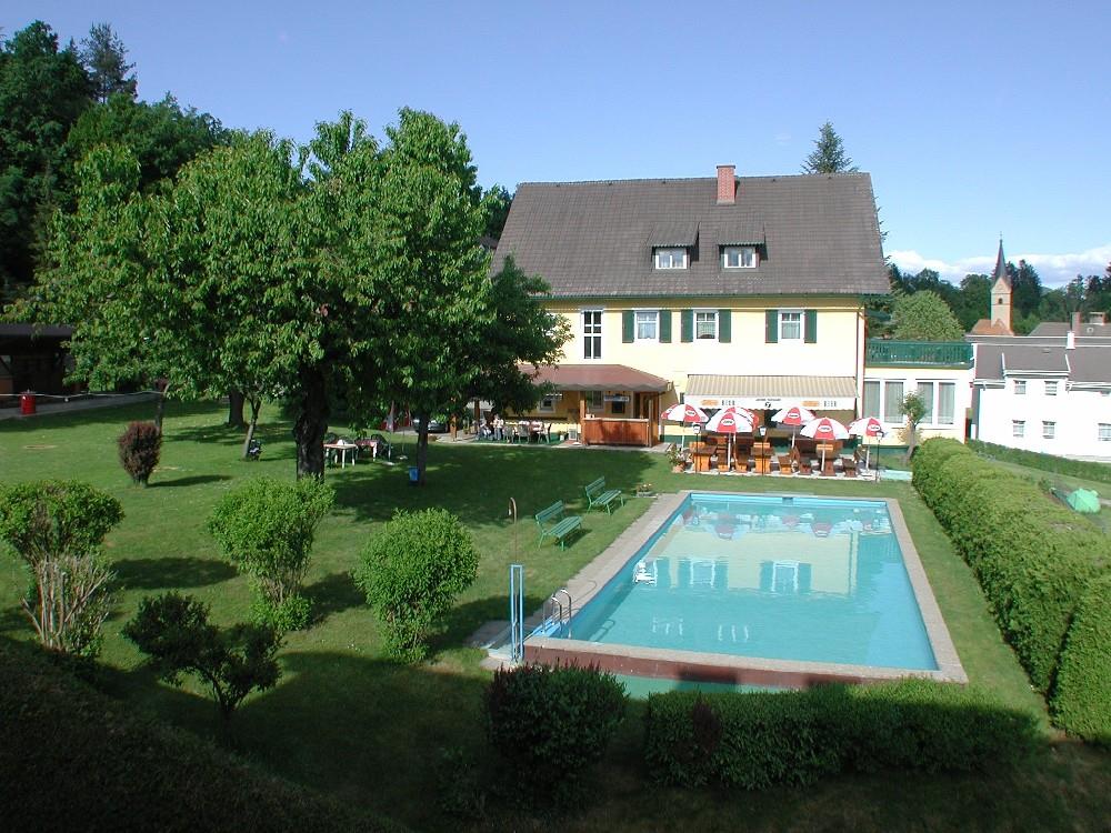 A beautiful house with a green garden and a swimming pool. There are loungers and umbrellas for the guests.