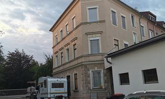 A multistory building on a quiet street. In the background, trees and a cloud formation are visible.