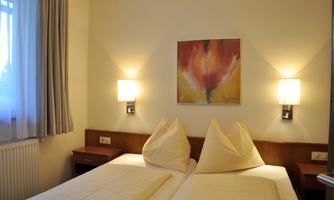 A simple bedroom with two beds and real pillows. An abstract picture hangs on the wall, and there are two bedside lamps.