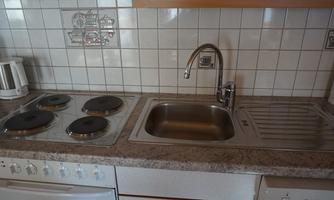 A modern kitchen with a stove, a sink, and countertop. The walls are tiled with white tiles.
