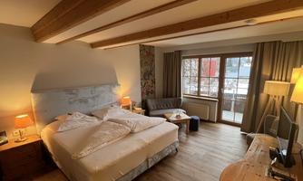 A cozy hotel room with a large bed, a sofa, and a desk. Large windows let in plenty of daylight.