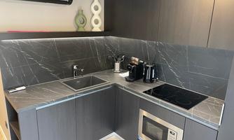 A modern kitchen with dark cabinets and an elegant stone countertop. The equipment includes a stove, a microwave, and various kitchen appliances.