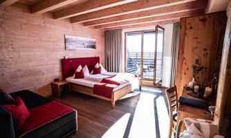 A cozy room with wood paneling and a large window. The bed is neatly decorated with red cushions and there is a seating area.