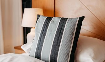 A cozy bedroom with a bed and a striped pillow. Next to the bed stands a lamp.