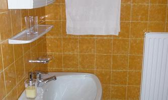 A small bathroom with yellow tiles and a white sink. A towel hangs on the wall, and a glass of juice sits on the sink.