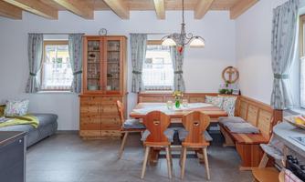 A cozy kitchen with a wooden table and chairs. Naturalistic elements and windows with curtains create an inviting atmosphere.