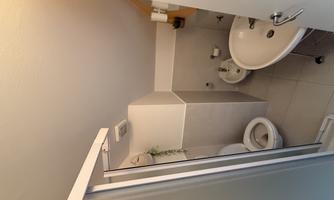 A small bathroom with a shower, toilet, and sink. The walls are bright and the atmosphere feels friendly and clean.