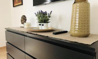 A modern sideboard with a beautiful flower arrangement and a decorative vase. In the background, there is a TV on the wall.