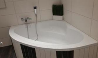 A modern corner bathtub with an elegant white surface. In the background, there is a plant pot with green decor.