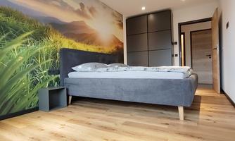 A modern bedroom with a large bed and a decorative mural of a landscape. The floor is made of light wood, and the walls are painted in neutral colors.