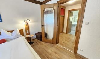 A cozy room with a large bed, a nightstand, and a chair. The door leads to a bathroom and another room.