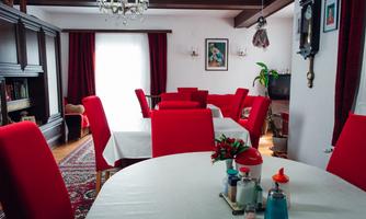 A cozy dining area with red chairs and a round table. The walls are simply decorated, and there is a lot of natural light.