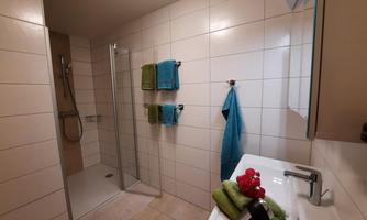 A modern bathroom with a shower and a sink. Colorful towels and fresh bath towels are arranged.