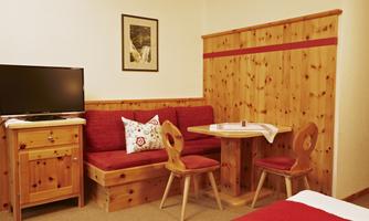 A cozy room with wooden furniture, a television, and a small table with chairs. The sitting area is decorated with red cushions.