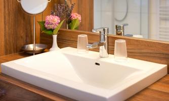 A modern sink made of white materials with an elegant faucet. In the background, decorative accessories and plants can be seen.