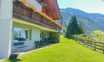 A charming house with a balcony full of flowers. The well-maintained garden and the mountains in the background create an idyllic atmosphere.