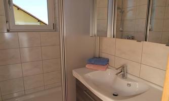 A modern bathroom with a shower and a sink. There are light tiles and a mirror above the sink.