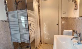 A modern bathroom with a glass shower and a white sink. The walls are tiled, and there is a large mirror above the sink.