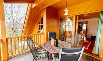 A cozy balcony with a table and chairs. The walls are painted orange and there is a view of greenery.