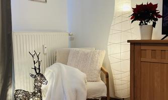 A cozy living space with a comfortable armchair and a white blanket. Next to the armchair stands a decorative lamp and a glowing deer made of wire.
