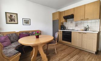A cozy kitchen with a round dining table and a seating area. The wooden furniture and colorful cushions create an inviting atmosphere.