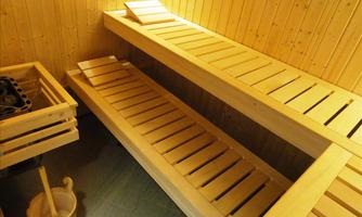 A sauna facility with wooden loungers and walls. Next to the loungers stands a bucket and a ladle.