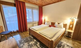 A cozy bedroom with wooden furniture and two beds. There are curtains in front of the windows and a beautiful view outside.