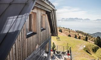 A wooden house with an impressive view of the mountains. The terrace is equipped with chairs and tables, perfect for a break in nature.