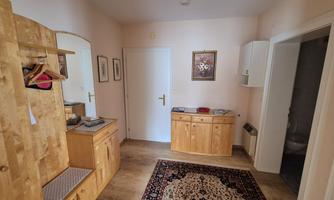 A cozy hallway with wooden furniture and a carpet. Some pictures hang on the wall and there is space for a wardrobe.