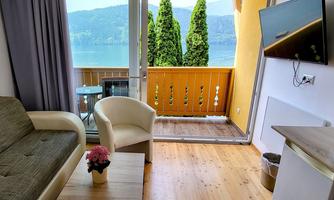 A cozy living room with a view of a lake. The room has large windows, a balcony, and modern furniture.
