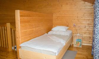 A cozy bedroom with wood paneling and a single bed. There is a small lamp and some books in a wooden box.