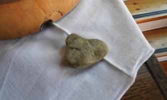A heart-shaped stone lies on a white cloth. In the background, a wooden bowl is visible.