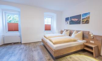 A modern bedroom with two beds and wooden furniture. There are windows with shutters and pictures on the wall.