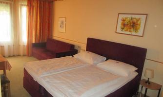 A cozy room with a double bed and a sofa.  
Large windows flood the space with light and there is a small bedside table.