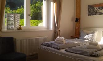 A bright bedroom with two beds and fresh towels. Light is shining through the window and green trees are visible outside.
