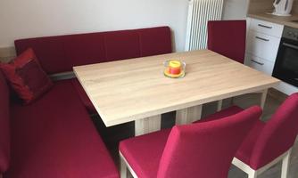 A dining area with a modern wooden table and red upholstered furniture. A candle in a glass sits on the table.