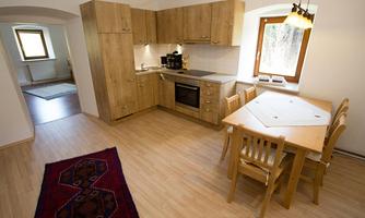 A modern kitchen made of light wood with an adjacent dining area. The room has large windows that let in plenty of light.