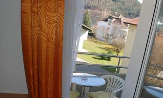 A balcony with a table and two chairs offers a view of the mountains. The interior is visible through an orange curtain.