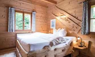 A cozy bedroom with wood paneling and a large bed. The room has windows with curtains and a bright, inviting atmosphere.