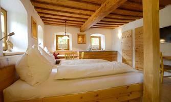 A cozy bedroom with a wooden ceiling and two comfortable beds. Large windows let in plenty of light and create an inviting atmosphere.